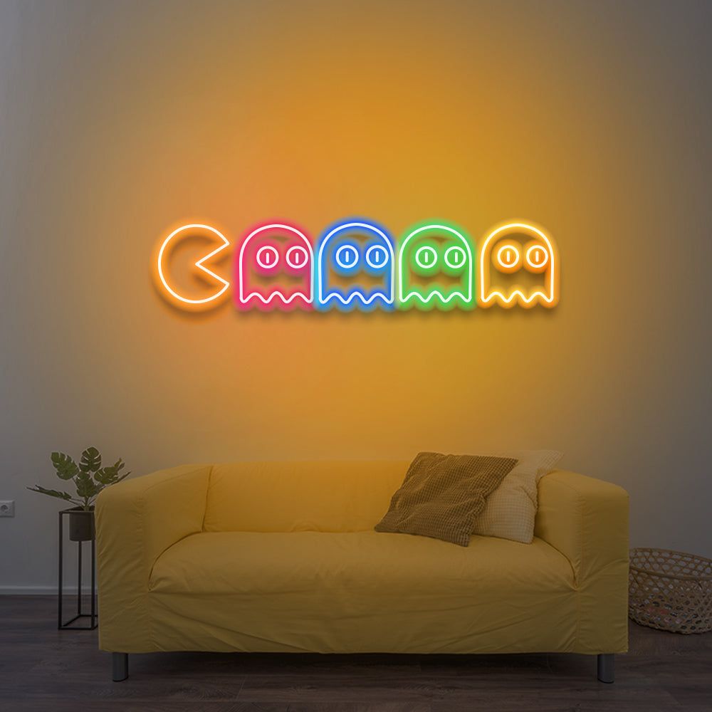 Pac Man Neon Sign – Custom Neon Sign for Kids Living Room 30 By 15 Inches Neon Pac-Man ghosts sign on a wall above a yellow couch.