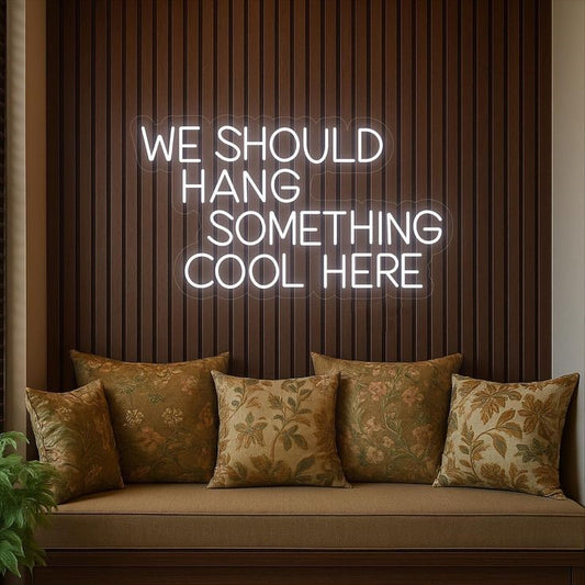 We should hang Neon Sign – Custom Neon Sign for Living Room Neon sign with text 'WE SHOULD HANG SOMETHING COOL HERE' above a sofa with patterned cushions.