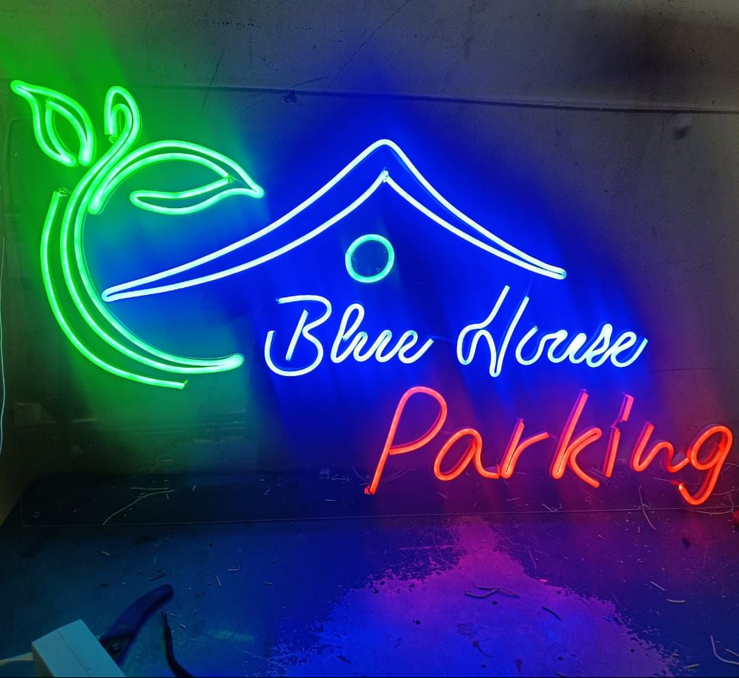 Neon sign with 'Blue House Parking' text and colorful design on a wall.