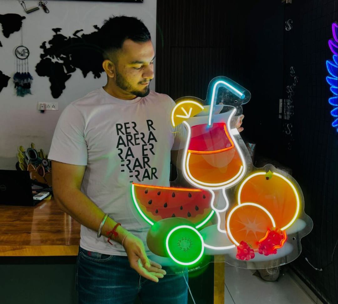 Man holding a neon sign with fruit and drink design in an indoor setting