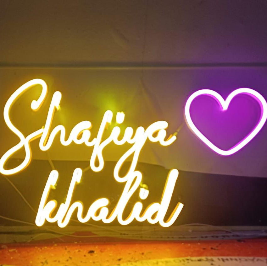 Neon sign with 'Shafiya Khalid' and a heart symbol on a dark background