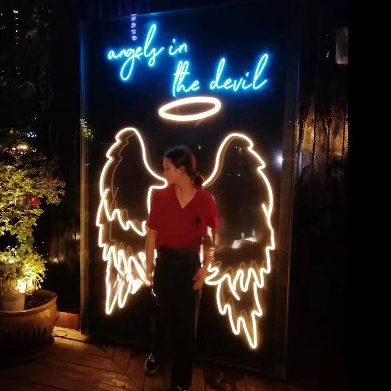 Angel Wings Neon Light for Wall Decors | Big Large Size Angel Wings Neon Light for Selfie Point | Custom Neon Sign (48 by 48 inches) Person standing in front of a neon sign with angel and devil designs and the text 'angels in the devil'.