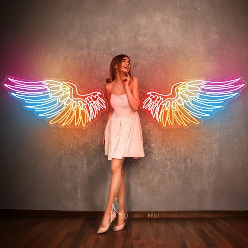 Angel Wings Neon Light for Wall Decors | Big Large Size Angel Wings Neon Light for Selfie Point | Custom Neon Sign (30 by 60 inches) Woman in a white dress standing between neon rainbow wings on a textured wall.