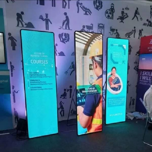 Boost branding with a 32" touch-enabled LED video standee for advertising & marketing. Smart signage for retail, events, promotion & interactive digital display. Promotional display with digital screens showing images of people and text on a wall with silhouettes.
