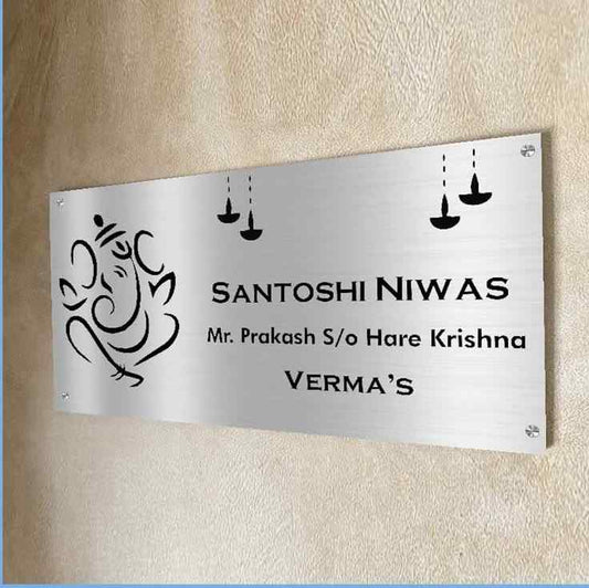 Custom metal home name plate with Lord Ganesha artwork, family surname, and elegant black lettering mounted on a wooden entrance wall.