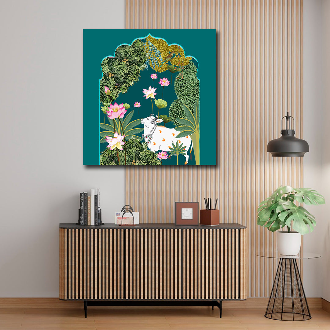 Canvas Painting Wall Frame | Traditional Indian Pichwai Cow Art | Sacred Kamdhenu with Pink Lotus in Teal Arch Modern Wall Art Decors (24x24 Inches) Decorative painting of a cow among flowers and foliage on a wall above a wooden cabinet.