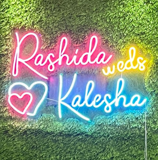 Couples Name Neon Light | Handmade Neon Décor for Couple’s Room Neon sign with colorful text and heart on a grassy background