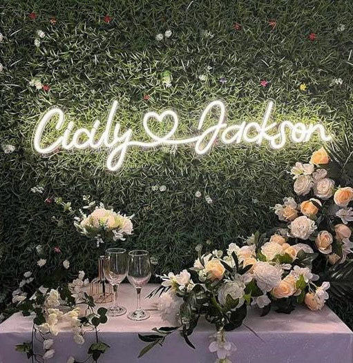 Couples Name Neon Light | Romantic Wall Neon Light Decoration Neon sign with 'Cicily Jackson' on a grassy background with floral decorations.