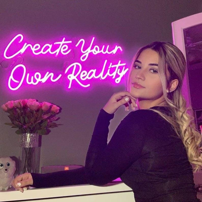 Pink Create Your Own Reality neon wall sign with cursive lettering for home decor