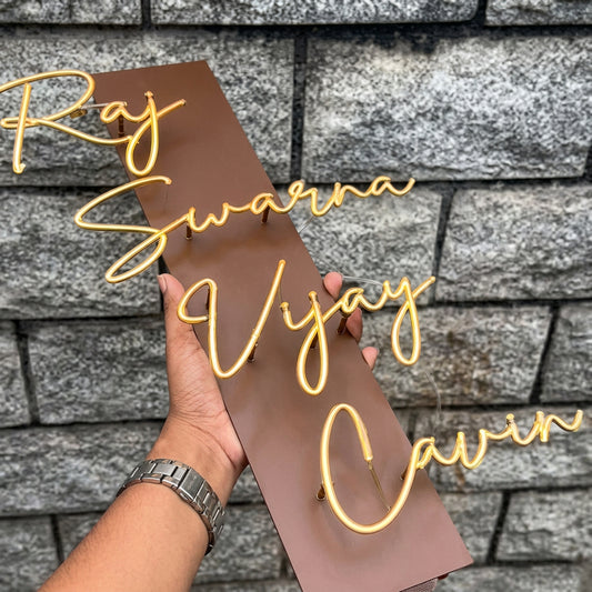 Luxury personalised family name sign with raised gold cursive lettering on a slim brown plaque, displayed on modern stone and wooden entrance walls.