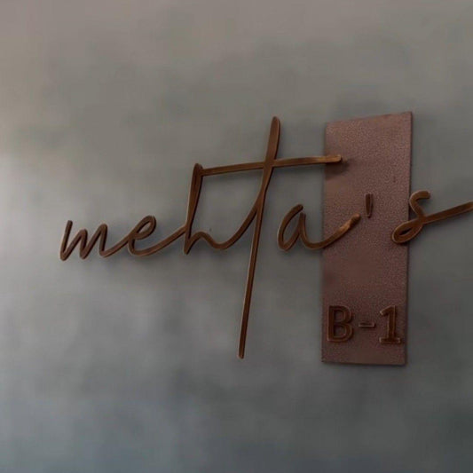 Luxury personalized metal house name sign featuring cursive family lettering and a matching address number on an exterior wall.