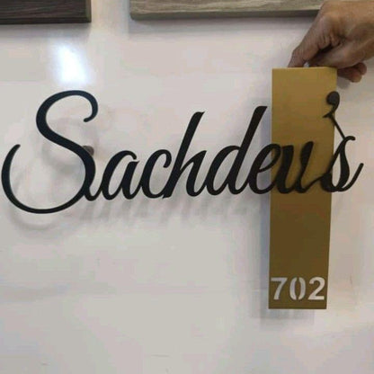 Modern personalised family name sign with raised black script lettering and a gold house number plate mounted on a contemporary entrance wall.