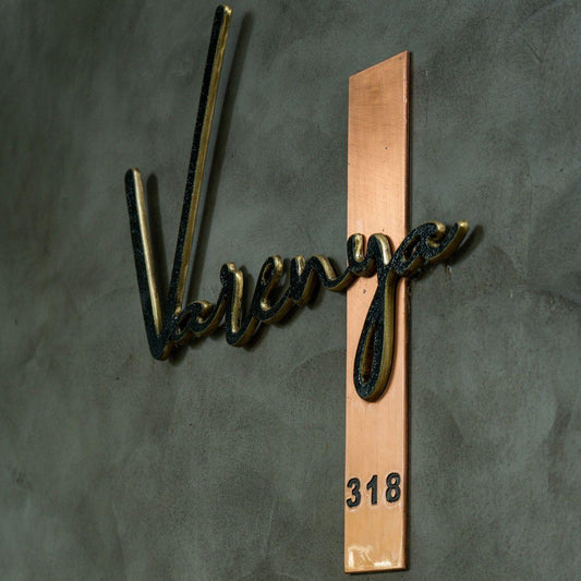 Modern personalised house name sign with raised black script lettering and a copper address panel, displayed on stone and textured exterior walls.