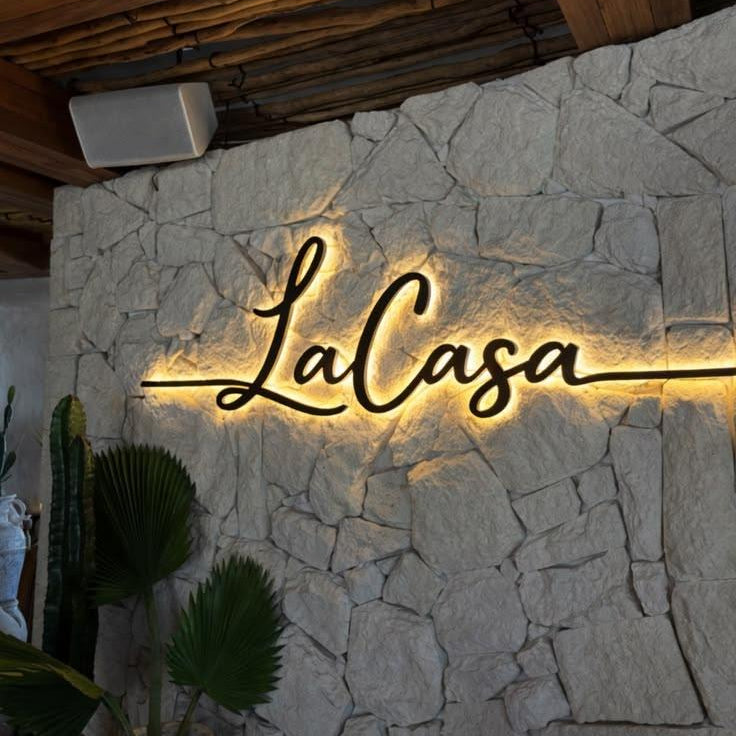 Modern illuminated house name sign with personalised cursive lettering and warm LED halo lighting mounted on a wooden wall and contemporary outdoor entrance.