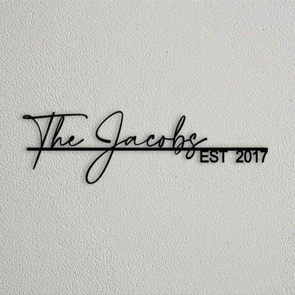 Modern personalized metal wall name sign with elegant cursive family lettering and establishment year mounted on textured stone and plaster walls.