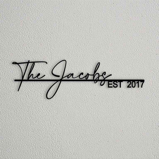 Modern personalized metal wall name sign with elegant cursive family lettering and establishment year mounted on textured stone and plaster walls.