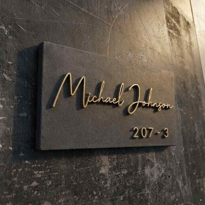 Modern personalized black wall nameplate with gold 3D-style family name lettering and custom apartment number mounted on marble and wooden entrance walls.
