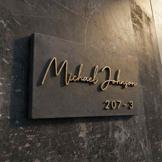 Modern personalized black wall nameplate with gold 3D-style family name lettering and custom apartment number mounted on marble and wooden entrance walls.