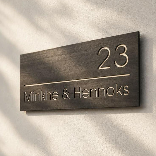 Modern rectangular black wood-effect house number sign with minimalist gold lettering, personalised family names, and a contemporary entrance wall display.