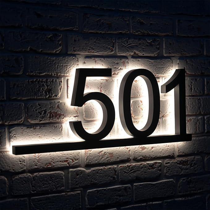 Modern 3D house number 501 address plate with glowing warm halo illumination, displayed on stone and neutral plaster entrance walls.