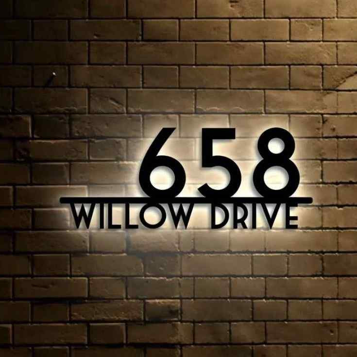 Modern LED house address plaque with raised black numbers and street name, mounted on a luxury home's exterior brick entrance.