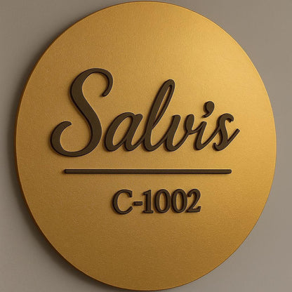 Luxury circular gold metal name plate with personalised family name, black 3D script lettering, and apartment number mounted on a modern wooden entrance door.