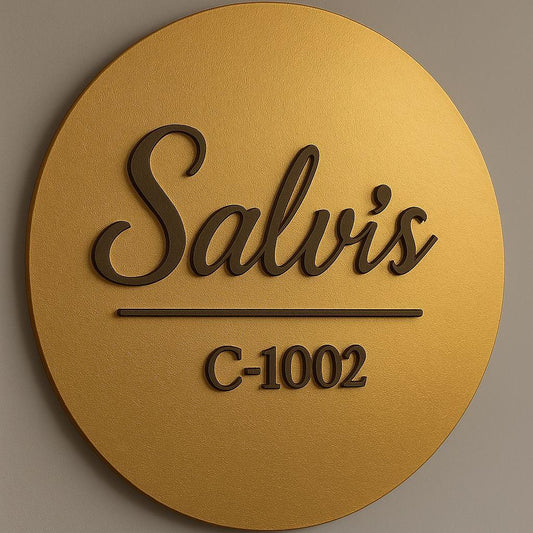 Luxury circular gold metal name plate with personalised family name, black 3D script lettering, and apartment number mounted on a modern wooden entrance door.