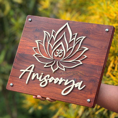 Premium rectangular wooden entrance name board with gold 3D lotus and Om design, custom family name, and four metallic corner fixings mounted on a modern home wall.