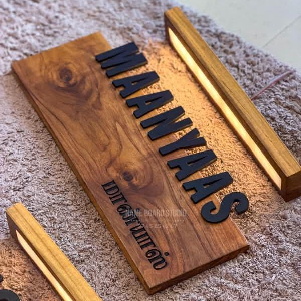 Premium teak-tone wooden entrance name sign with black raised letters and integrated-style warm lighting on a modern exterior wall.