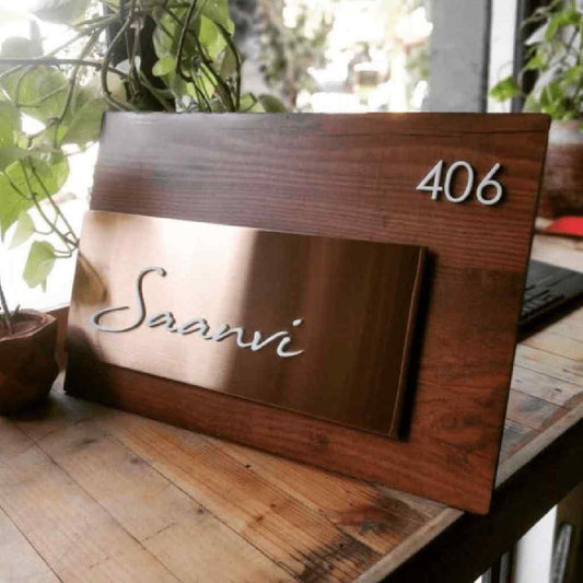 Premium personalized wooden entrance name board with a gold-finish nameplate displaying Saanvi and a white apartment number on a walnut background.