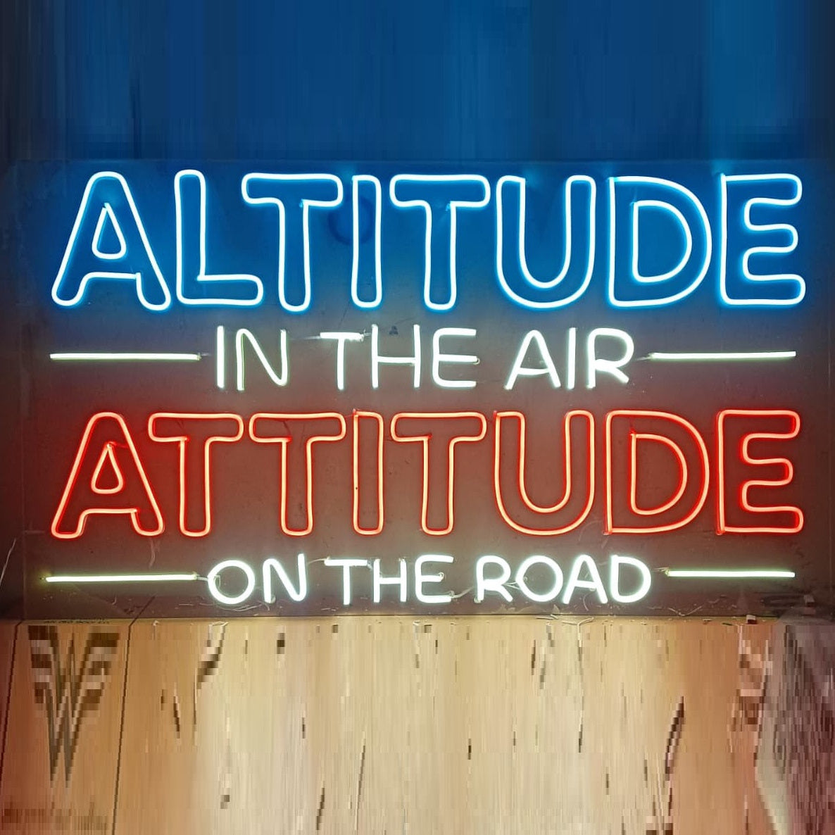 Customized Neon Name Sign | LED Neon Light for Couples, Weddings & Birthdays Neon sign with motivational quote 'Altitude in the air, attitude on the road' against a blue curtain.