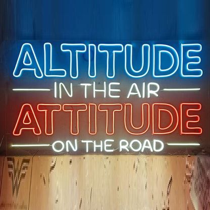 Customized Neon Name Sign | LED Neon Light for Couples, Weddings & Birthdays Neon sign with motivational quote 'Altitude in the air, attitude on the road' against a blue curtain.