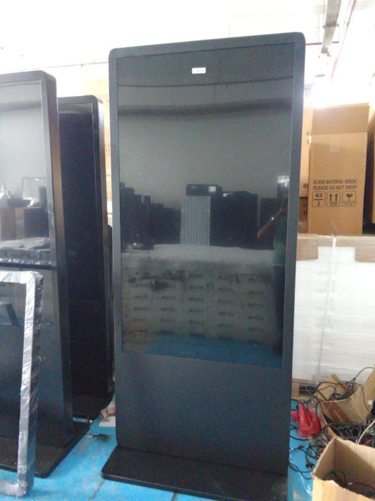 LED Digital Standee Video Display Signage Touch Screen for Branding, Advertising | Digital Advertising Display Screen | Led Video Standee 32" I Type - Touch Screen Large black screen device on a stand with boxes and other equipment in the background