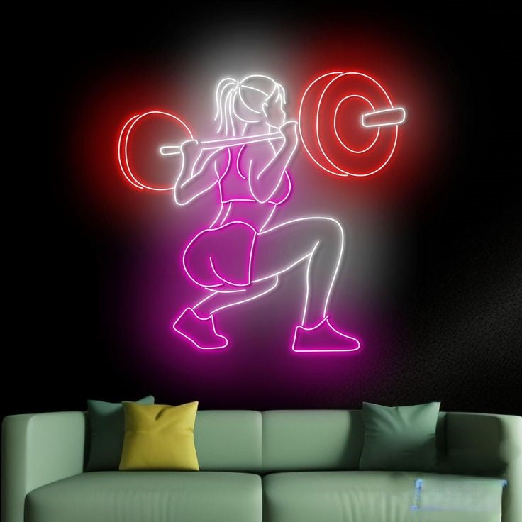 Girl Uplift Barbell Neon Sign | Custom Neon Sign | Neon for Gym Decoration Sign Neon sign of a woman lifting weights on a dark wall above a green sofa.