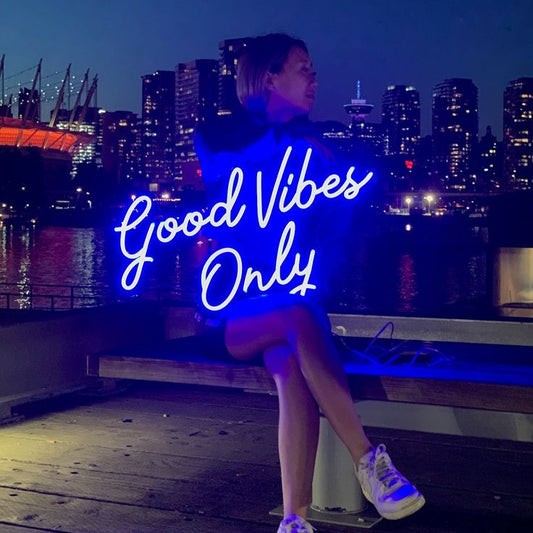 Good Vibes Only Neon Sign | Custom Neon Sign | Neon for Living Room Person sitting on a dock with 'Good Vibes Only' neon sign and city skyline in the background