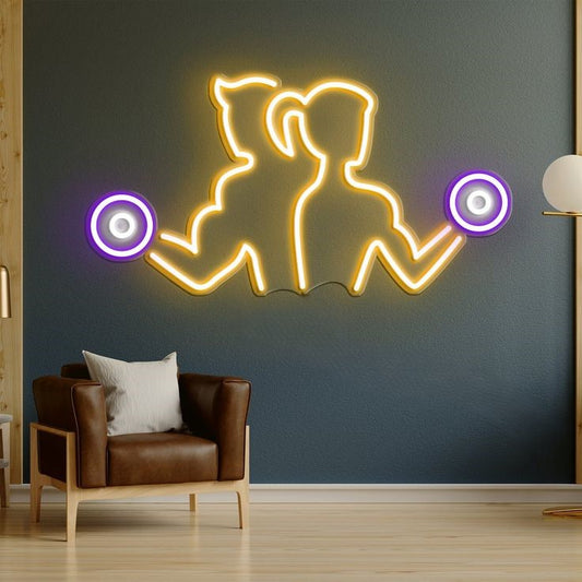 Gym Couple Neon Sign | Custom Neon Sign | Neon for Gym Decoration Sign Neon light art of a couple holding hands on a dark wall with a brown leather chair below.