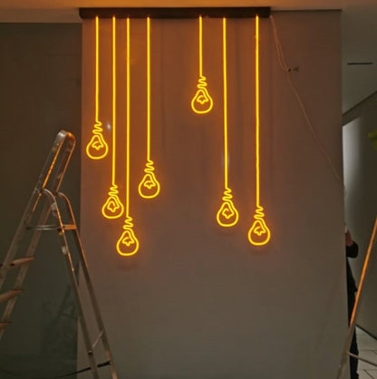 Hanging Bulb Neon Sign | Custom Neon Sign | Neon for Living Room Decor Neon light bulb shapes hanging on a white wall with a ladder in the foreground.