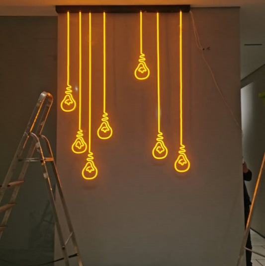 Hanging Bulb Neon Sign | Custom Neon Sign | Neon for Living Room Decor Neon light bulb shapes hanging on a white wall with a ladder in the foreground.