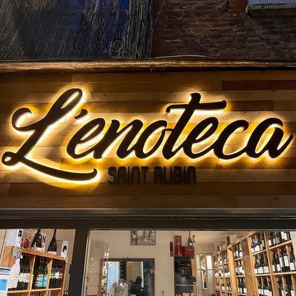 Neon sign of 'L'Enoteca Saint Aubin' on a wooden facade with interior view.