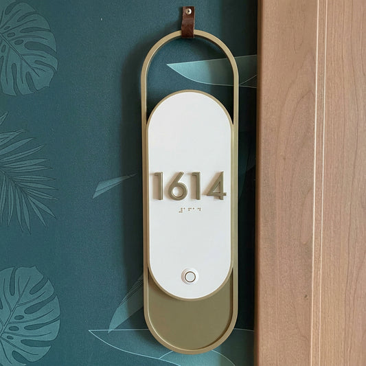 Elegant oval house number sign with gold-tone frame and olive green base displayed on a modern entrance wall