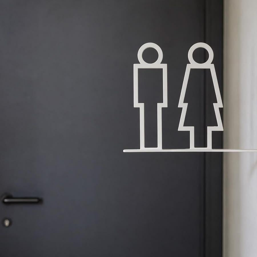 Minimalist white toilet signage with male and female pictograms on a projecting wall-mounted bracket displayed against beige stone, wooden and grey textured walls.
