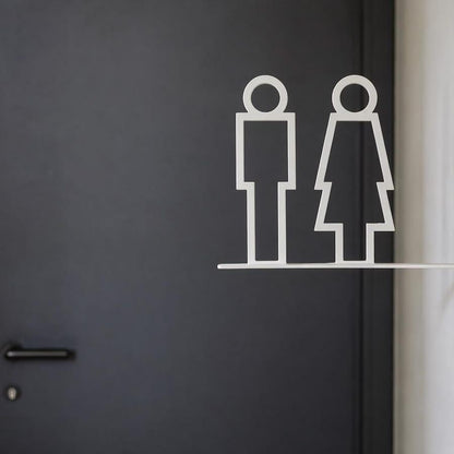 Minimalist white toilet signage with male and female pictograms on a projecting wall-mounted bracket displayed against beige stone, wooden and grey textured walls.