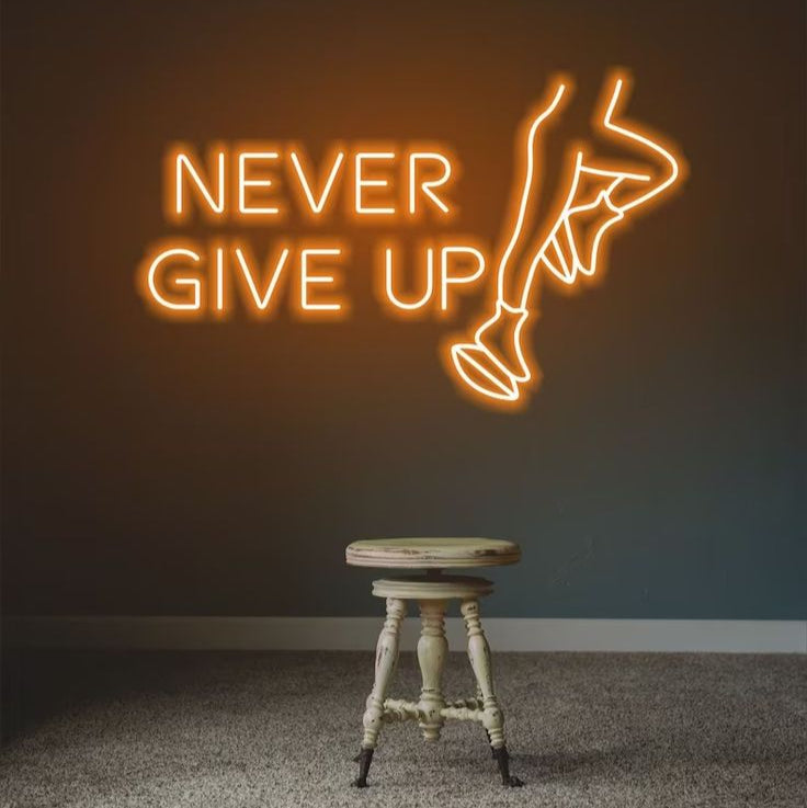 Never Give Up Neon Sign | Custom Neon Sign | Neon for Gym Wall Decor Neon sign with 'Never Give Up' and a silhouette of a person on a dark wall with a stool in the foreground.