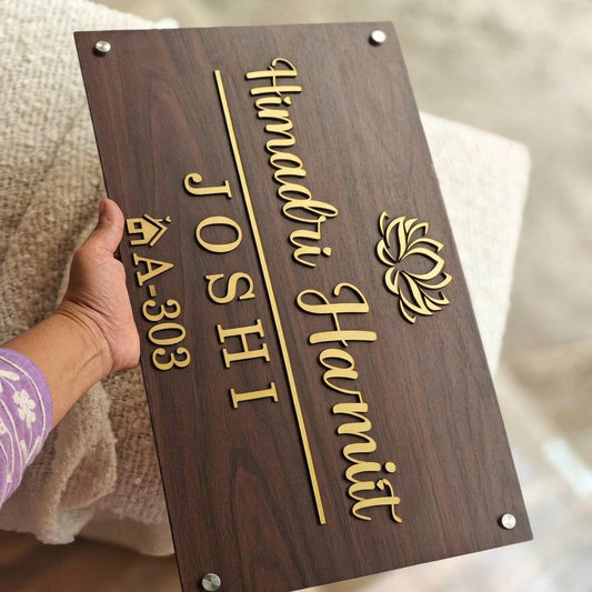 Custom rectangular family name plate featuring elegant gold lettering, a lotus symbol and flat number on a brown wood-grain background, displayed on a contemporary wall.