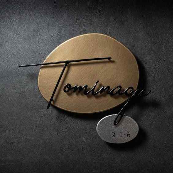 Modern gold circular family nameplate with black cursive lettering and a custom silver-tone number plate mounted on a home entrance wall.
