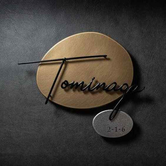 Modern gold circular family nameplate with black cursive lettering and a custom silver-tone number plate mounted on a home entrance wall.
