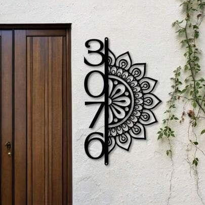Decorative black house number wall sign with artistic mandala detailing and vertical numerals displayed on textured stone and neutral exterior walls.