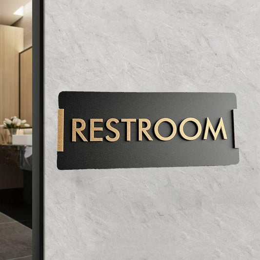 Modern brushed gold washroom signage with male and female pictograms displayed on wooden, beige marble and textured grey walls.