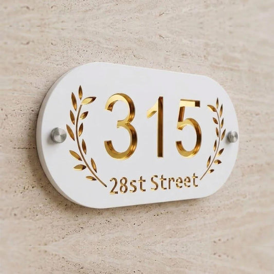 Modern white and gold address number sign mounted on a wooden entrance wall, featuring metallic gold numerals and elegant leaf detailing.