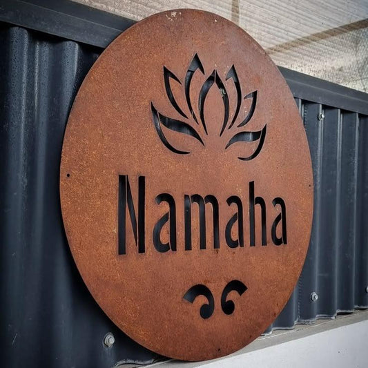 Custom circular rustic metal name board featuring a decorative lotus motif, black lettering, and earthy brown finish mounted on a contemporary stone exterior wall.
